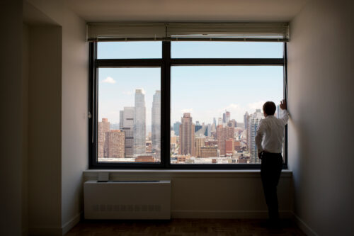 man standing looking out window in apartment