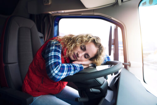 Sleepy and tired female truck driver sleeping over steering wheel