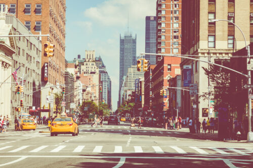 New York City street road in Manhattan at summer time, many cars, yellow taxis and busy people walk to work.
